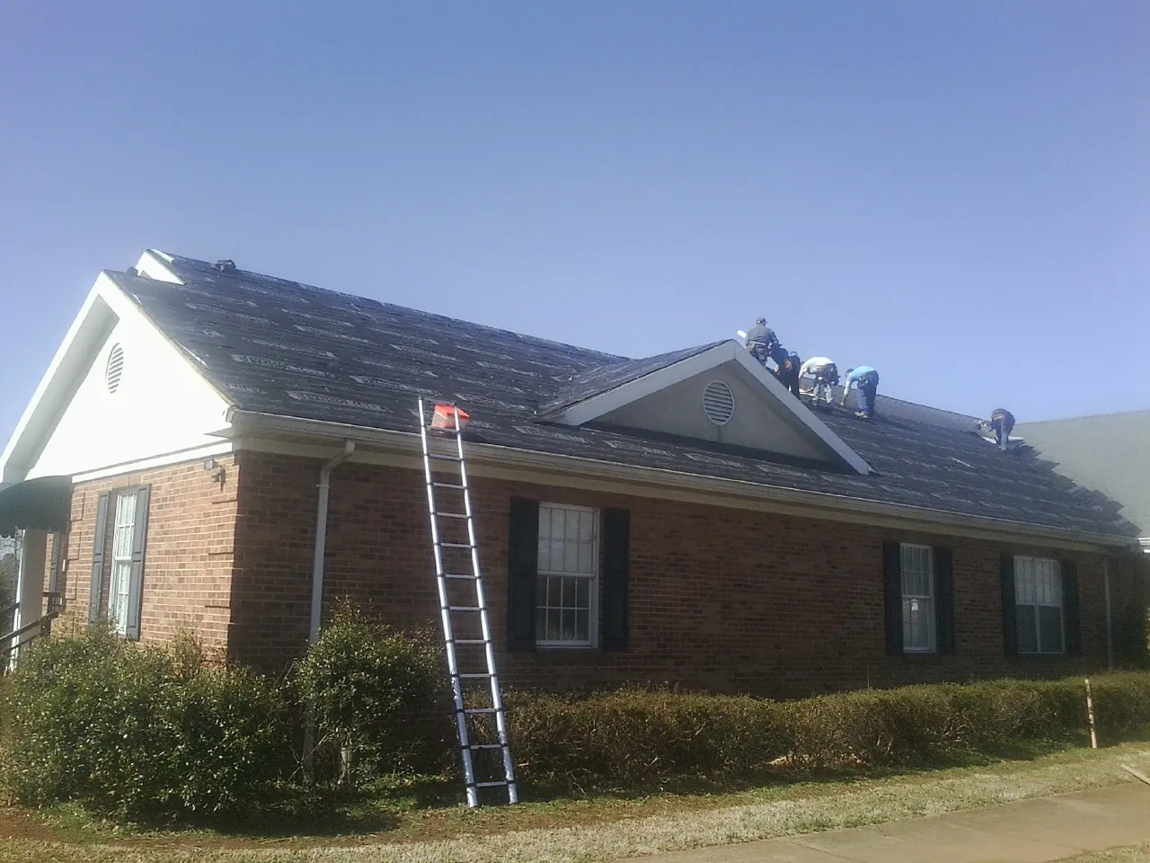 Crew tearing shingles off a brick ranch roof with a ladder set — Emergency Roof Repair work by our crew in Springboro