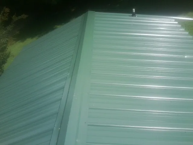 New green metal panels meeting at the ridge of a roof — Flat Roof Repair work by our crew in Springboro