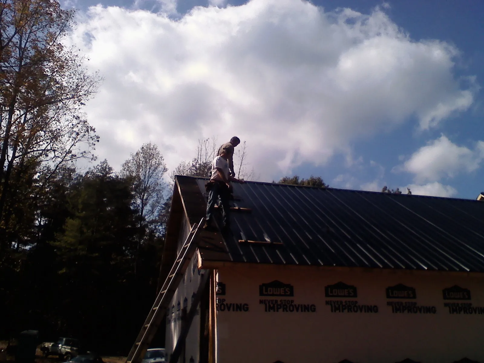 Roofer fastening dark metal panels high against a cloudy sky, from a Roof Inspection job in Springboro